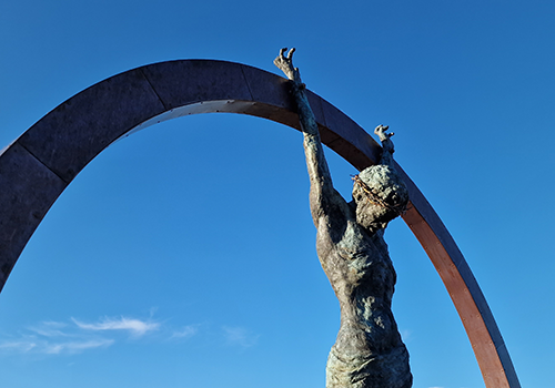 Photograph of metal sculpture of a man with a crown of thorns nailed to an arch by his wrists